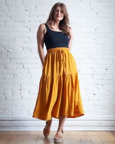 a woman standing in front of a white brick wall wearing a black top and yellow skirt