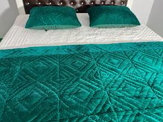 a bed with two pillows and green blankets on it's headboard in a bedroom