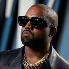 a man with sunglasses and a chain on his neck looking off to the side while standing in front of a blue background