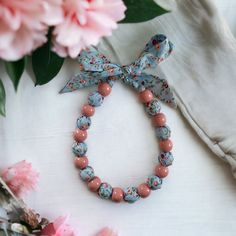 Blue and pink floral fabric and pink painted wooden beaded necklace. Handmade in Devon, England. Made from fabric and 21 wooden beads (11 outside and 10 inside the fabric). The overall length from the ends of the fabric is approximately 110cm Designed to be worn by fastening the fabric into a bow, allowing you to wear it at the length best suited for your look.  Please note that as these are painted beads some slight paint marks may be present. Pink Wooden Beaded Necklaces For Gifts, Pink Wooden Beads Necklace For Gift, Necklace Fabric, Painted Beads, Devon England, Fabric Necklace, Bow Necklace, Wood Necklace, Necklace Statement