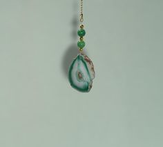 a piece of jewelry hanging from a chain on a gray wall with green bead