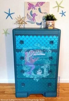 a blue dresser with mermaid design painted on the drawers and under it is a starfish painting