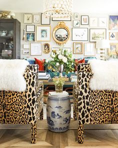 two leopard print chairs in front of a table with flowers and pictures on the wall