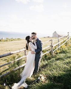 a bride and groom kissing in front of a fence on their wedding day at the farm