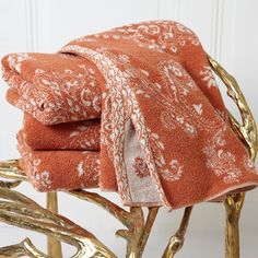 two towels folded on top of each other in front of a gold chair with branches