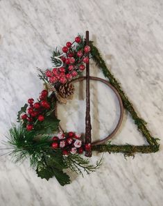 a triangle made out of branches and flowers on top of a marble floor with a pine cone