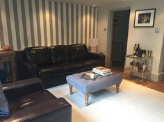 a living room with black leather furniture and striped walls