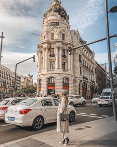 a woman crossing the street in front of a large building with a dome on top