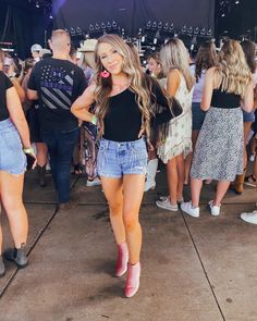 a group of people standing around at a music festival with one woman wearing short shorts