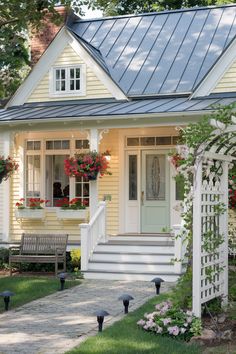 a small yellow house with white trim and flowers on the front door, steps leading up to it