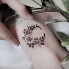 a woman's hand holding onto a tattoo with flowers on the side of her arm