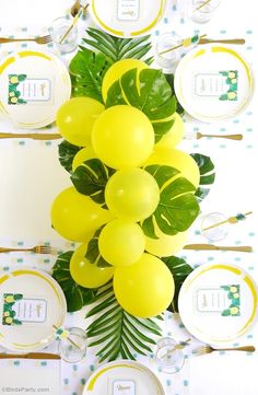 the table is set with yellow balloons and green leaves