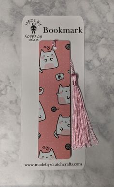 a pink bookmark with cats on it and a tassel hanging from the front