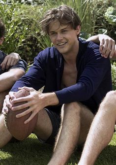 two young men sitting on the grass with one holding a football in his right hand