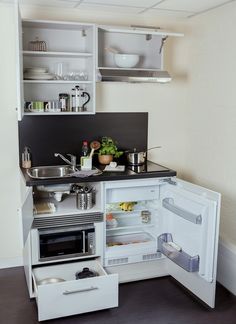 an open refrigerator with its door wide open in a small kitchen, next to a sink and stove