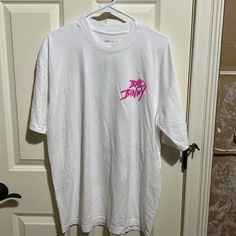 a white t - shirt with pink writing on it hanging from a hanger in front of a door