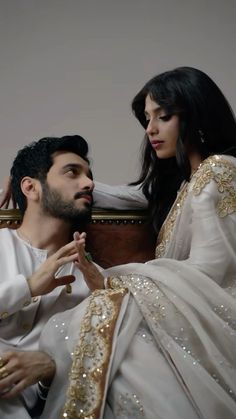 a man sitting next to a woman on top of a bed in a white dress