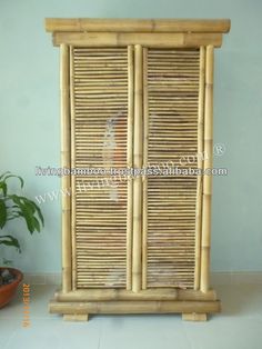 a bamboo cabinet with two doors and plants in pots on the floor next to it