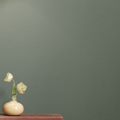 a vase with flowers sitting on top of a wooden table next to a green wall