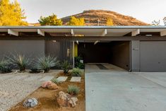 a modern home in the desert with large garages and graveled driveway leading up to it's front door