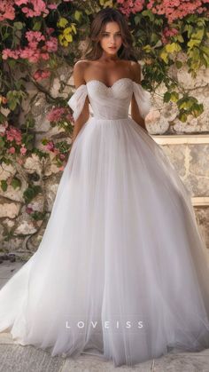 a woman in a white wedding dress standing next to a wall with flowers on it