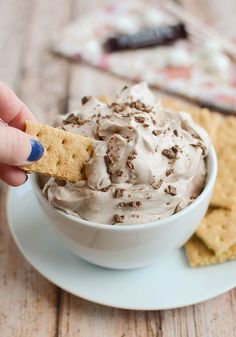 a hand holding a cracker over a bowl of ice cream