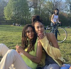 two young women sitting on the ground in a park, one is holding her hand up