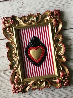 a gold frame with a red and black heart in it on a white wooden surface