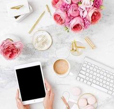 the woman is using her tablet on the desk with flowers and other items around her