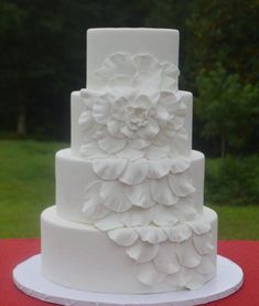 a three tiered white wedding cake with flowers on the top and bottom, sitting on a red table cloth