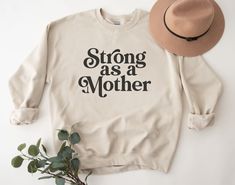 "Introducing the Strong As A Mother sweatshirt, the perfect addition to any cool mom's wardrobe. With the words \"Strong As A Mother\" emblazoned across the front, this sweatshirt is not only a statement of empowerment but also a celebration of motherhood. Whether you're a boy mom, a soccer mom, or just a proud mama, this sweatshirt is for you. Join the Cool Mom Club and show off your strength and femininity with this Strong Mama Shirt. Perfect for any strong woman or feminist mom, this sweatshirt is a must-have for anyone who wants to make a bold statement while staying comfortable and stylish. So why wait? Order your Strong As A Mother sweatshirt today and show the world that being a mother is a strength, not a weakness. Ideal for any situation, a unisex heavy blend crewneck sweatshirt i Relaxed Fit Tops With Lettering For Mother's Day, Mother's Day Cotton Sweatshirt With Slogan, Mother's Day Slogan Top With Relaxed Fit, Strong As A Mother, Mom Wardrobe, Club Dance, Dance Mom, Moms Club, Strong Woman