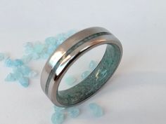 two wedding bands with green and white marble inlays on a plain surface, surrounded by blue crystals