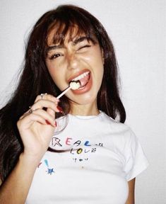 a woman brushing her teeth with a toothbrush in front of her face and wearing a white t - shirt