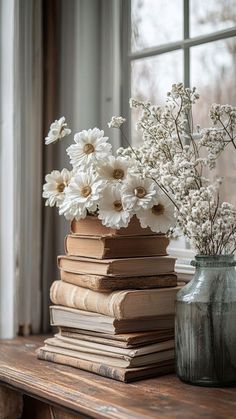 a stack of books sitting on top of a wooden table next to a vase filled with flowers