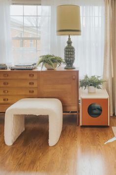 a living room with wooden floors and white curtains on the windowsills, a bench in front of a large window