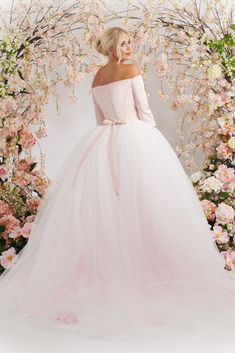 a woman in a pink wedding dress standing next to a floral arch with flowers on it