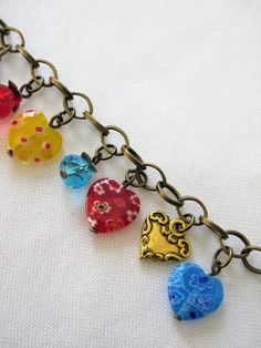 "This heart charm bracelet is made with multi-colored millefiori hearts, gold tone hearts, blue crystals, Czech faceted red glass and brass metals. It is adjustable along the chain from 7 to 8\". At random charms make each bracelet slightly different. This bracelet will be slipped into an organza bag and shipped in a bubble mailer." Multicolor Heart Charm Bracelet For Jewelry Making, Multicolor Heart Charm Bracelet, Multicolor Heart Charm Bracelet With Round Beads, Valentine's Day Multicolor Charm Bracelet With Heart Beads, Valentine's Day Multicolor Heart Beads Charm Bracelet, Multicolor Heart Beads Bracelet For Jewelry Making, Multicolor Metal Jewelry With Heart Beads, Multicolor Heart Bracelets For Jewelry Making, Heart-shaped Multicolor Bracelets For Jewelry Making