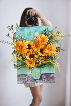 a woman holding up a painting with flowers in it