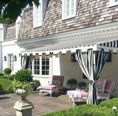 an outdoor patio area with chairs, tables and curtains on the side of the house