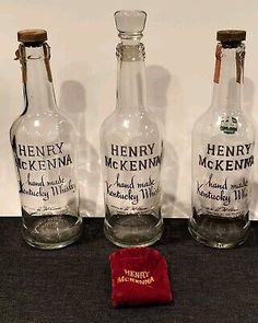 three empty bottles with labels on them sitting next to a red velvet pouch and paper bag