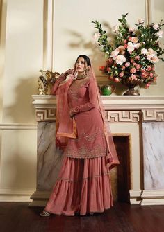 a woman standing in front of a fire place wearing a pink dress with gold embroidery on it