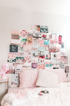 a white bed topped with lots of pink and white pillows next to a wall covered in pictures