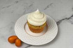 a cupcake with white frosting on a plate next to two tangerines