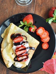 a black plate topped with crepes and strawberries