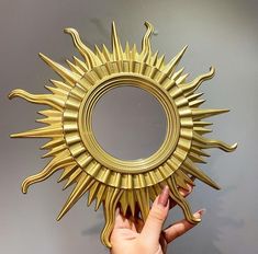 a person holding up a gold sun shaped mirror