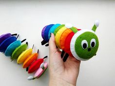 a hand holding a small stuffed caterpillar in front of a row of colorful ones