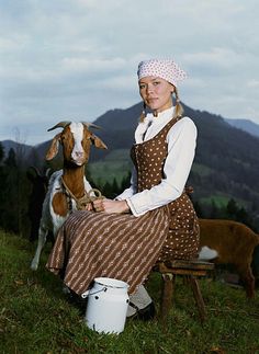 a woman sitting on a bench next to two goats