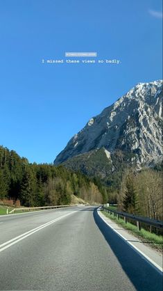 an empty road in front of a mountain with snow on the top and trees below