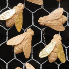 several wooden bees are hanging on a wire mesh fence, with gold leaf shaped decorations attached to them