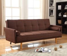 a brown futon couch sitting on top of a wooden floor next to a book shelf